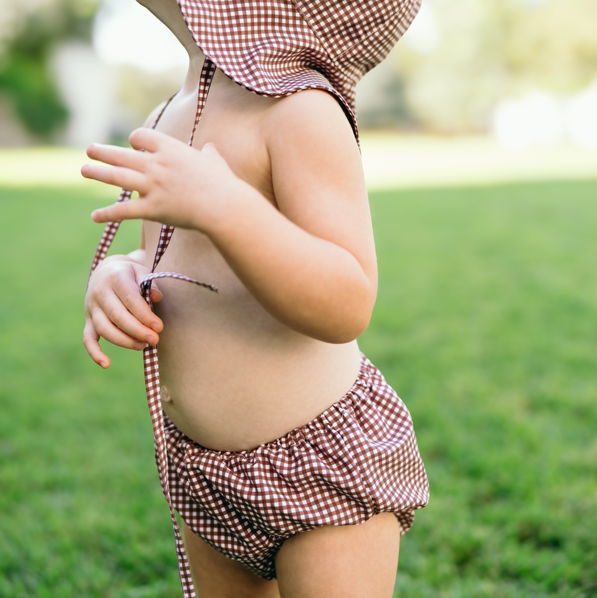 Side view of Baby Cocoa gingham diaper cover on toddler showing elasticized waist and leg openings with blurred grass