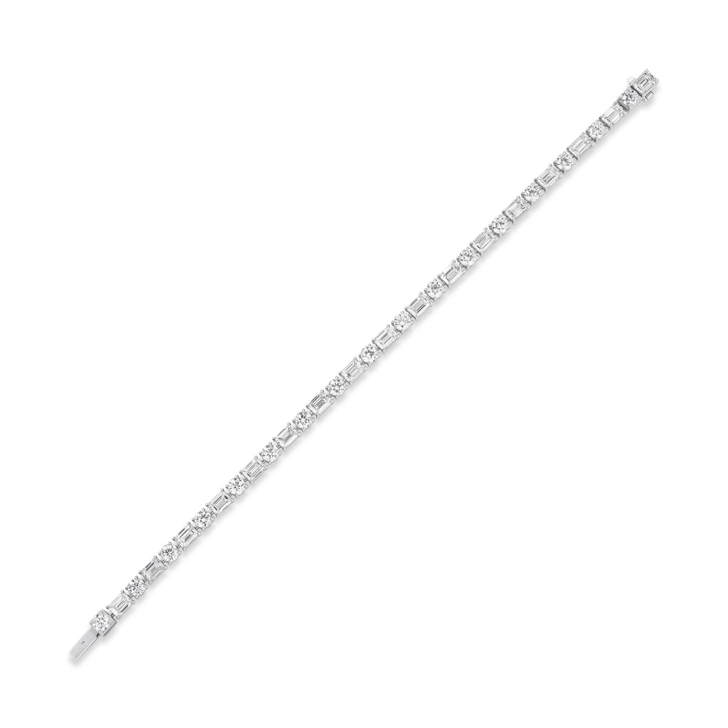 An Alternating East-West Set Round and Emerald Cut Diamond Tennis Bracelet in white gold, featuring sparkling diamonds set in a unique east-west pattern, elegantly displayed diagonally on a white background.