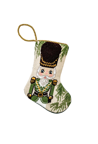 Hand-stitched needlepoint stocking featuring a nutcracker in green uniform with gold details and festive green accents