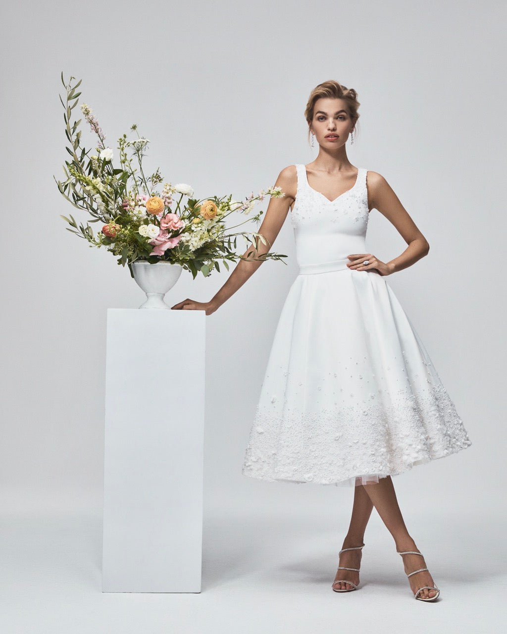 Front view of The Tara Skirt on a model showing a white tea-length A-line skirt with hand-embroidered pearls and fabric flowers