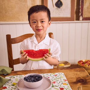 smiling boy eating fruit off pastel dishware