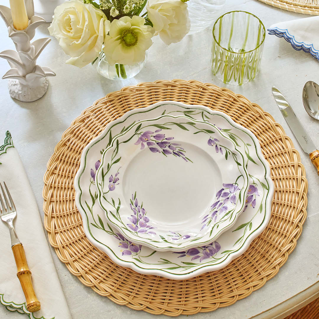 Top view of Wisteria Salad Plate showcasing handpainted purple wisteria flowers and scalloped edge on a woven placemat