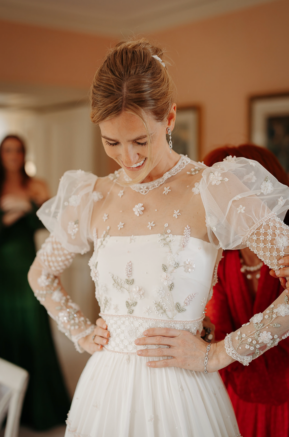 Bride smiling in a white floral-embroidered wedding dress with sheer puff sleeves indoors
