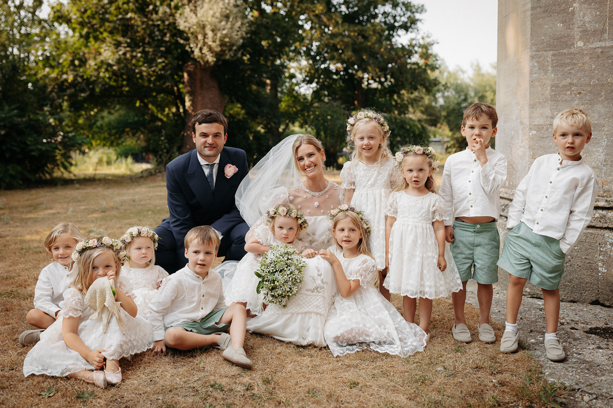 Ella May Sangster and Hughie de Zulueta pose with children at an outdoor wedding beside a stone building