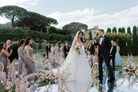 Bride and groom hold hands during an outdoor garden wedding surrounded by flowers, guests, and Villa Cimbrone