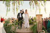 Paola Franssen and Guillermo Nieto walk through their Baja wedding ceremony surrounded by tropical greenery and cheering guests