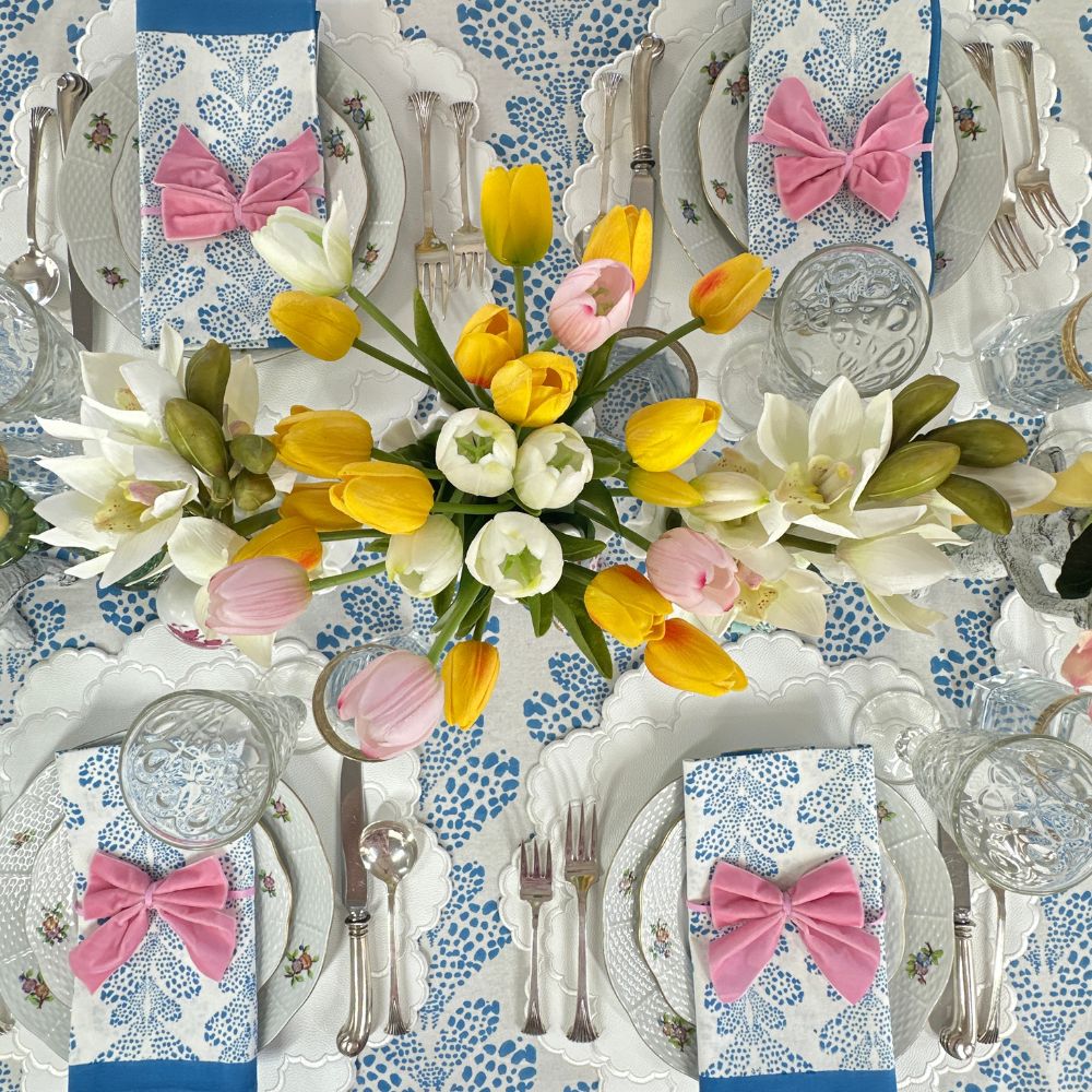 Easter-themed table setting with flowers, bow-knotted napkins, and decorative plates.