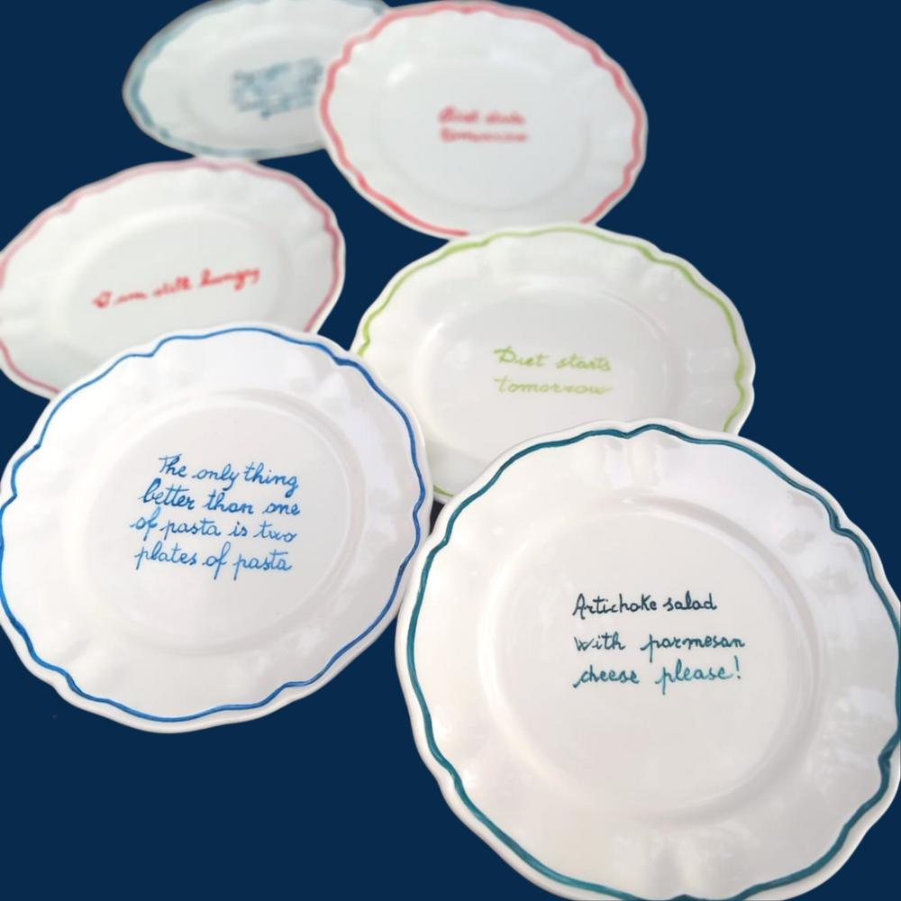 Angled overhead of six Recipe for Disaster scalloped plates with colored rims and handwritten menu phrases on dark background