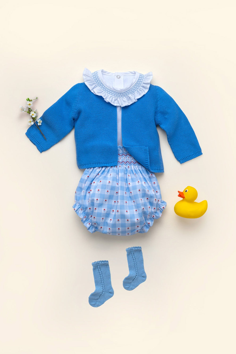 Flat lay of Lou bodysuit in Cloud White showing ruffled collar and hand smocked detail with blue cardigan and gingham bloomers