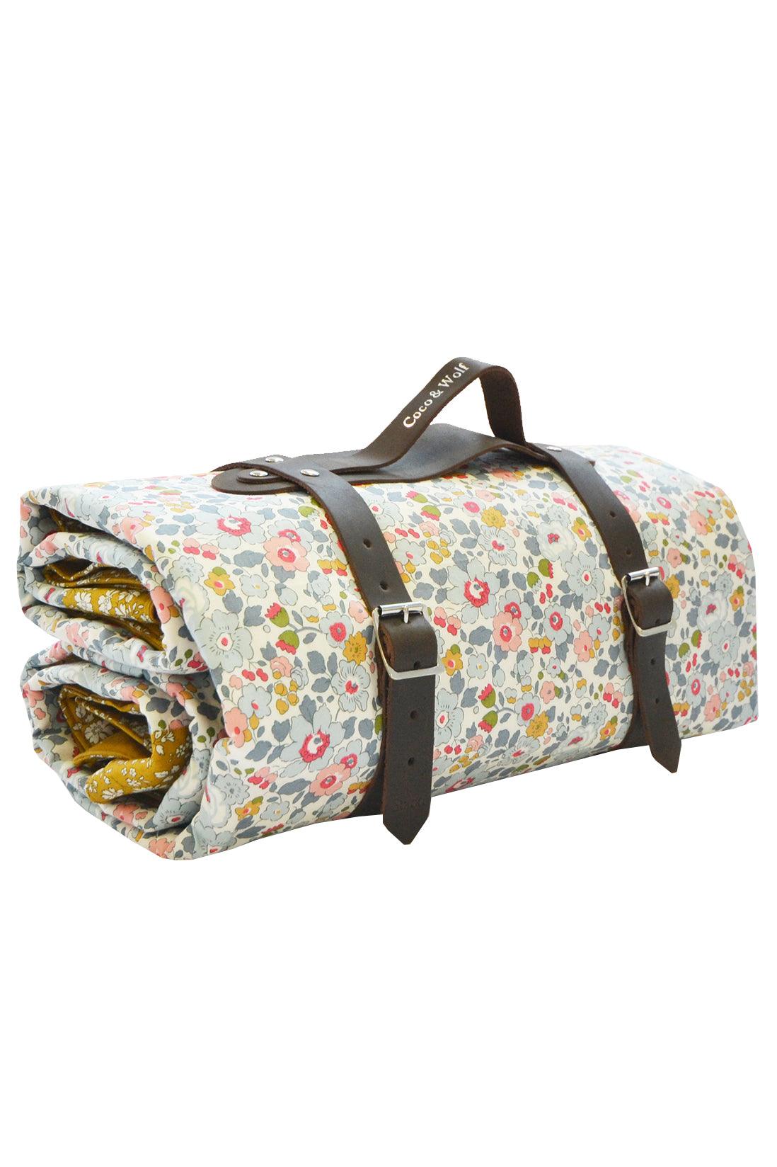 Front view of picnic blanket made with Liberty Fabric in Betsy Grey and Capel Mustard, with floral print and leather straps
