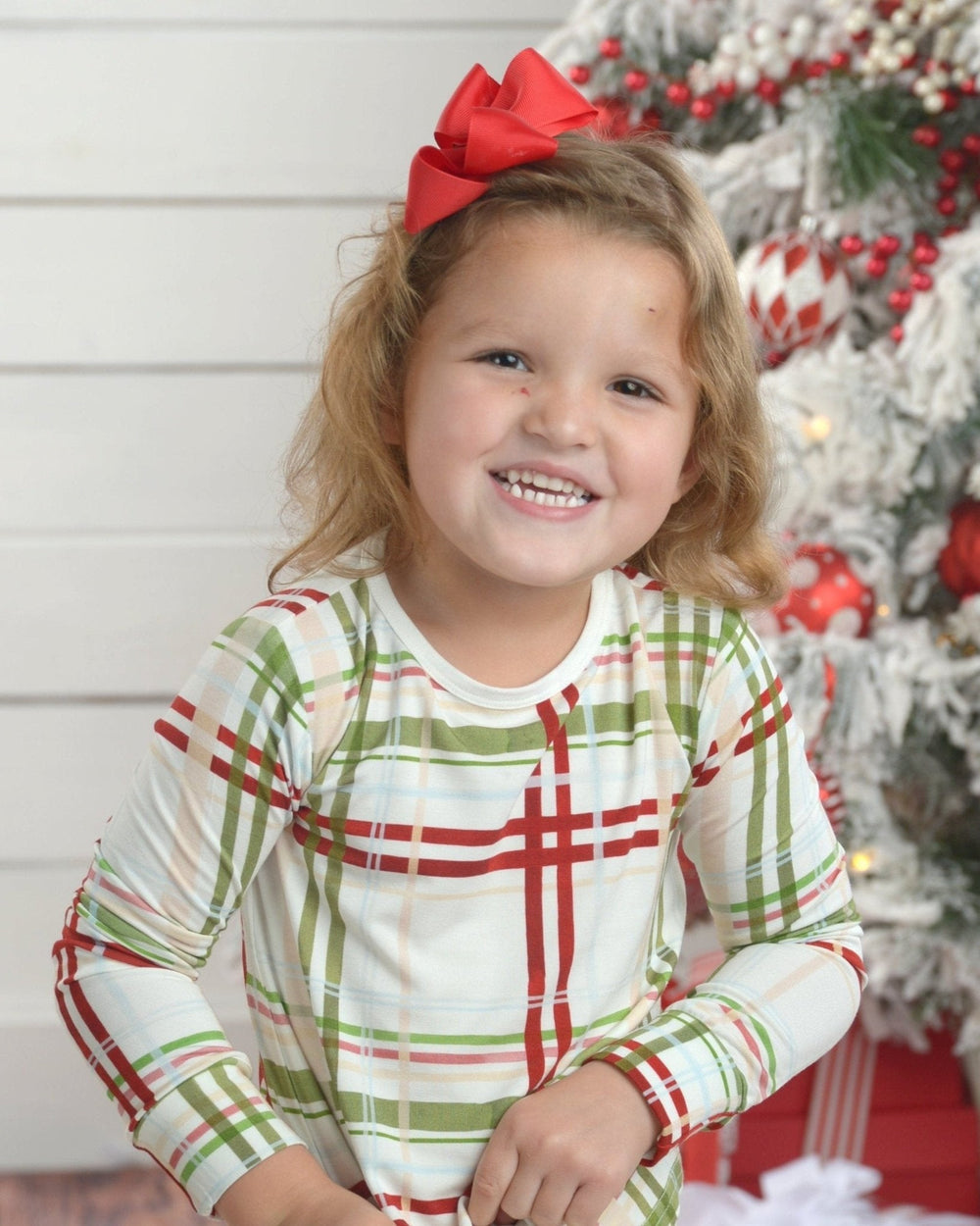 Front view of toddler wearing plaid bamboo two-piece pajamas showcasing long sleeves and matching pants with decorated Christmas tree background
