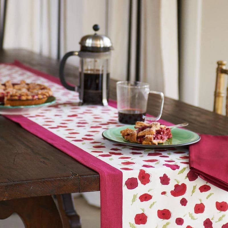 Angled view of Poppies Runner showcasing red poppies and delicate leaves on a dining table with coffee and pastries