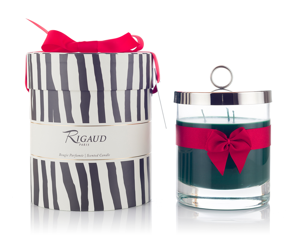 Front view of Rigaud Cyprès Prestige candle in glass with red ribbon beside striped gift box with red bow on white background