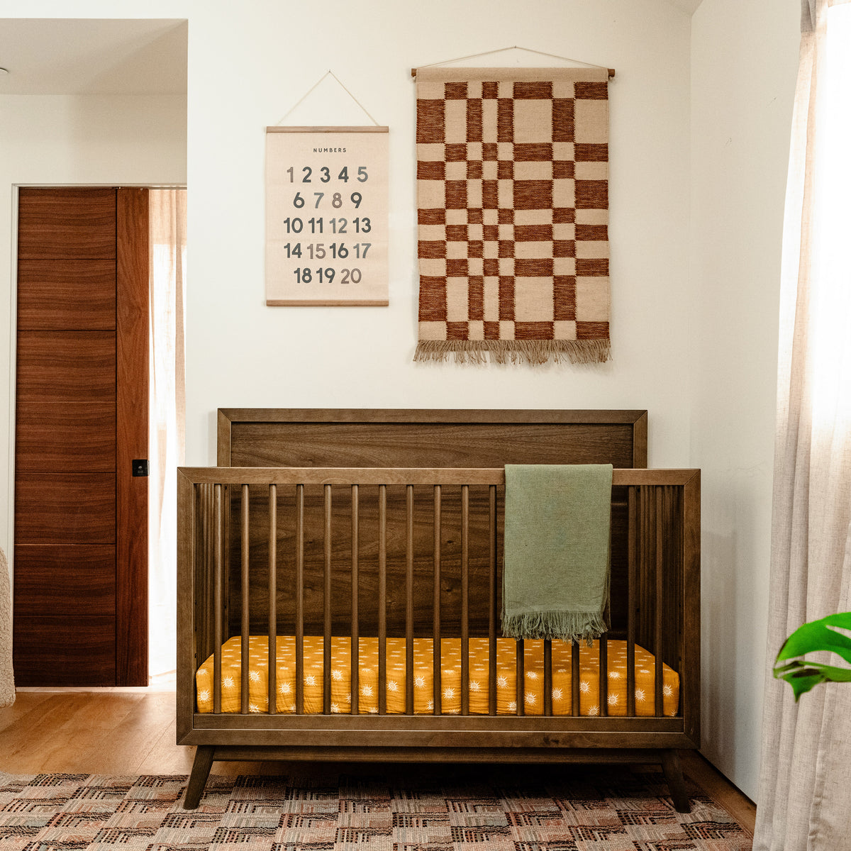 Front view of Palma 4-in-1 convertible crib in natural walnut showcasing high headboard and slatted sides in a nursery