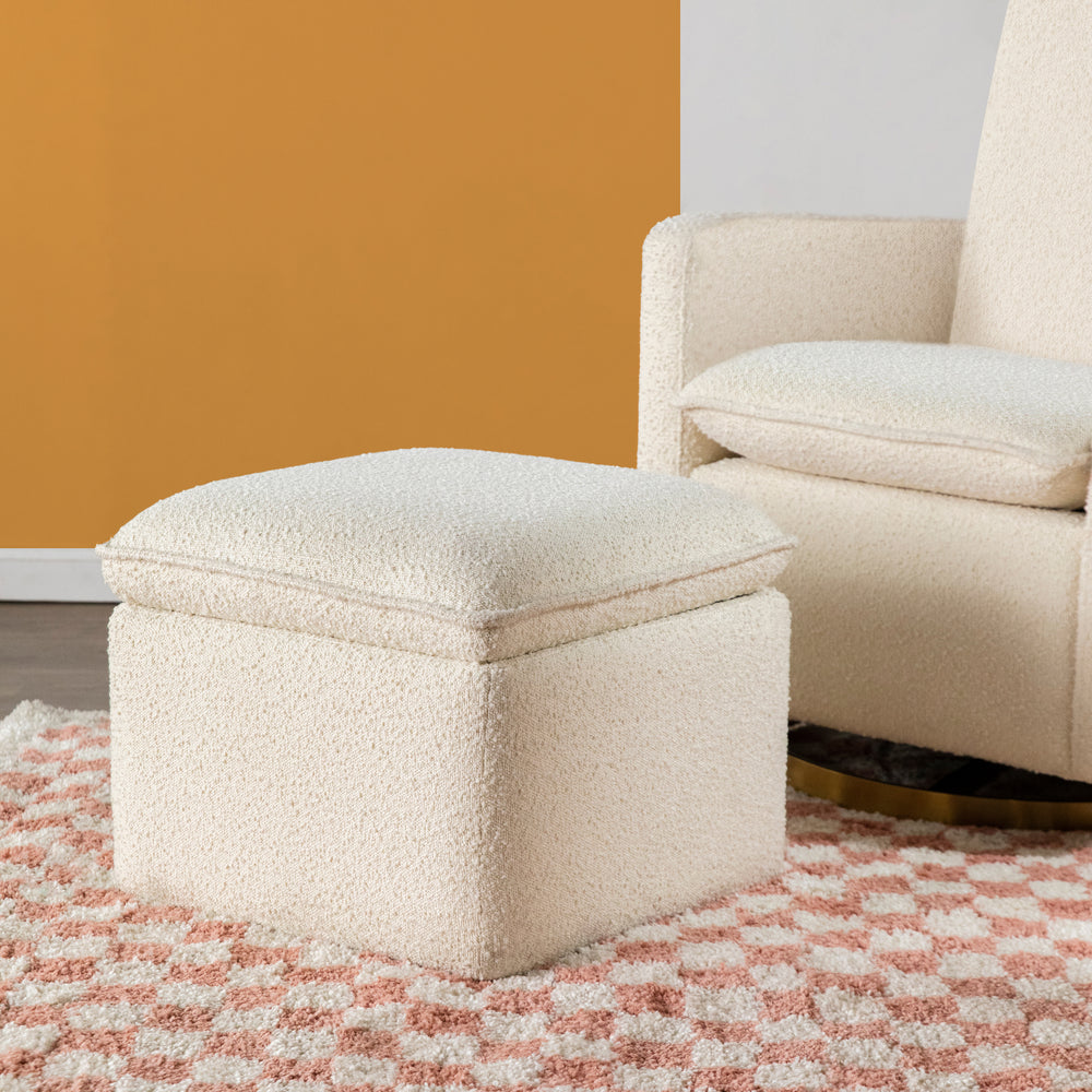 Three-quarter view of Cali storage ottoman in ivory boucle showing plush texture on pink check rug beside swivel glider
