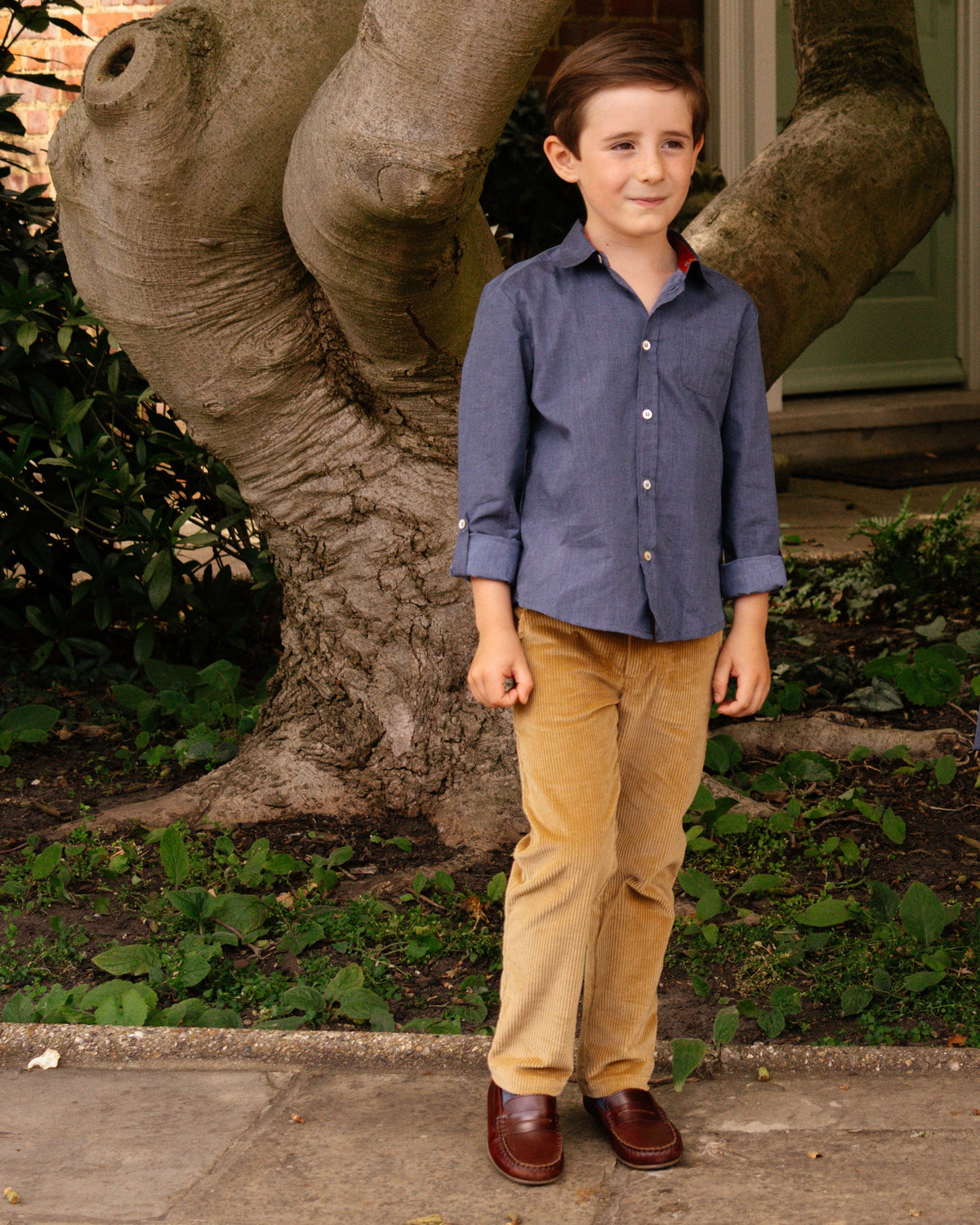 Young boy standing outdoors next to a large tree trunk