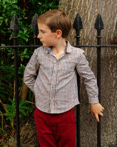 Young boy in a checkered shirt and red pants standing against a black metal fence.