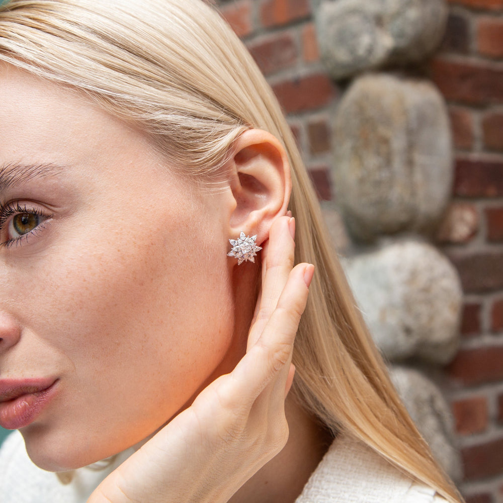 Close-up of left ear wearing Rosee Diamond Stud earring showcasing starburst pear- and square-cut diamonds in 18K white gold against brick background