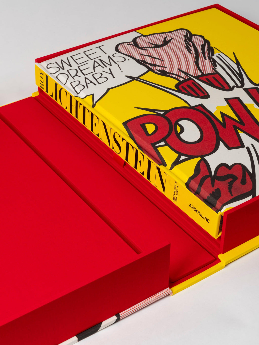 The Impossible Collection of Roy Lichtenstein by Assouline: Angled view of the book in its open red presentation box. The yellow cover shows SWEET DREAMS, BABY! in a comic speech bubble, POW! in red below, and a stylized dark-haired figure — all in Lichtenstein's pop-art style. Spine: ROY / LICHTENSTEIN in black on yellow. ASSOULINE at base.