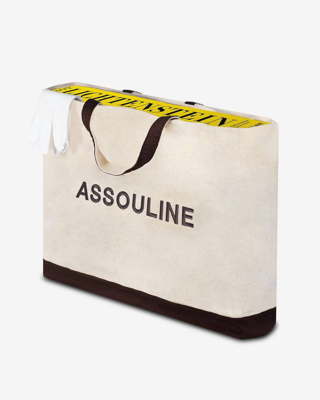 The Impossible Collection of Roy Lichtenstein by Assouline: A large cream canvas tote bag with dark brown handles and base trim. ASSOULINE is printed on the front in large dark brown sans-serif. The book's yellow spine with LICHTENSTEIN in large black vertical letters peeks above the bag opening alongside white cotton handling gloves.