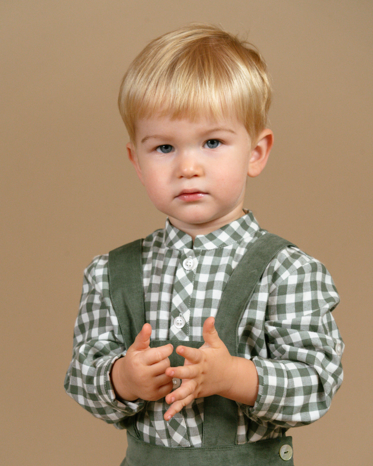 Child wearing a green checkered shirt and suspenders against a brown background