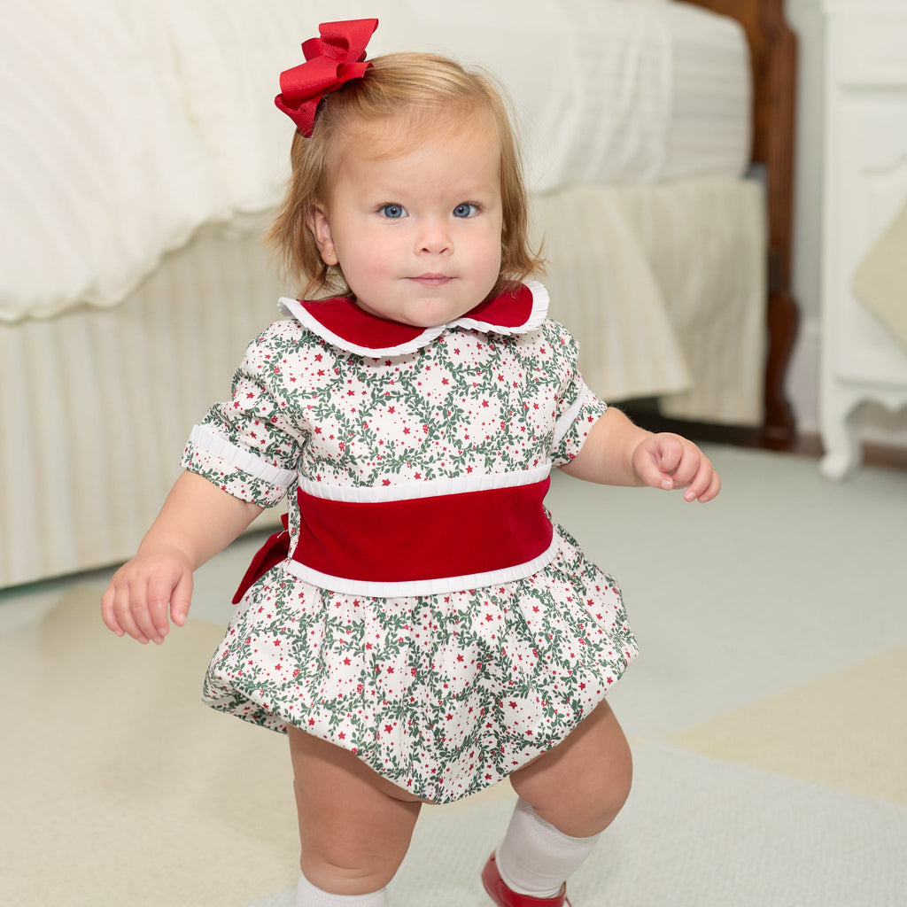 Grace Bubble in Regent Wreaths holiday print with red velvet sash and Peter Pan collar, finished with crisp white pleated trim for baby and toddler girls.