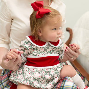 Grace Bubble in Regent Wreaths holiday print with red velvet sash and Peter Pan collar, finished with crisp white pleated trim for baby and toddler girls.