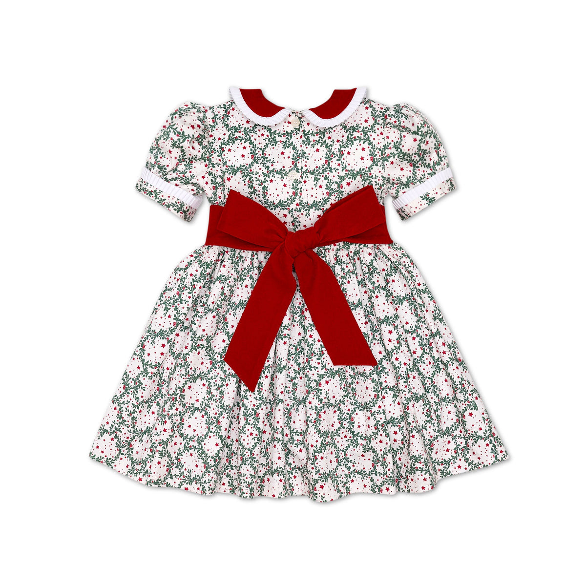 Girls’ holiday dress in Henry Duvall Regent Wreaths red and green Christmas print, featuring a red velvet Peter Pan collar and sash, white pleated trim, puff sleeves, and a full gathered skirt.