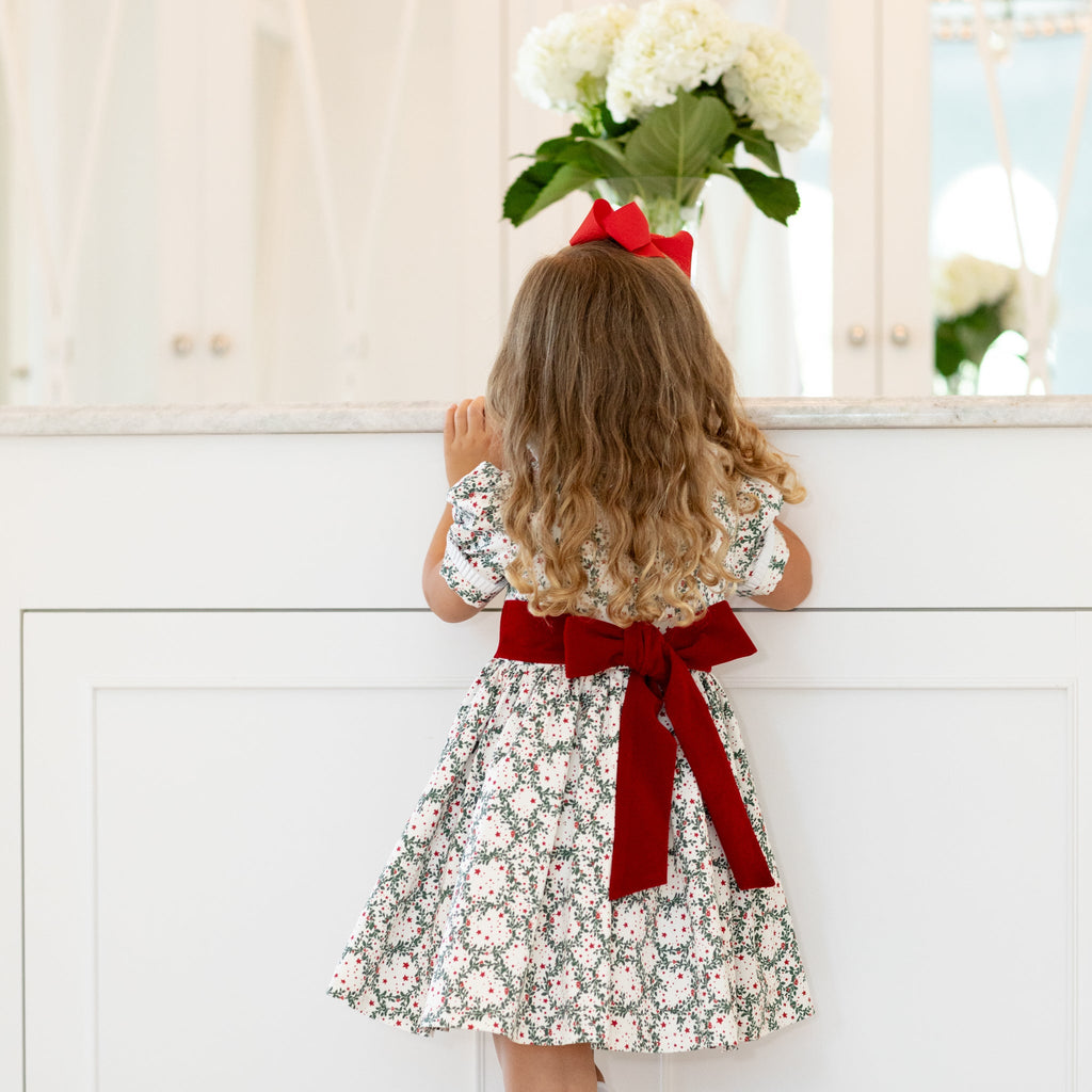 Back view of Short Sleeve Grace Dress in Regent Wreaths with red velvet sash and full gathered skirt against a white vanity