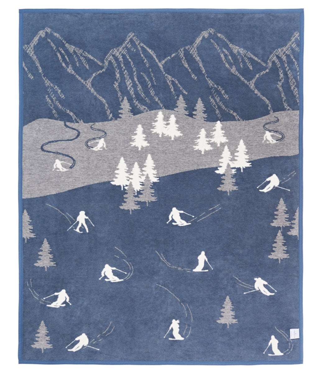 Blue blanket featuring mountains, ski slopes, skier silhouettes, trees, and winding ski tracks in white and gray.