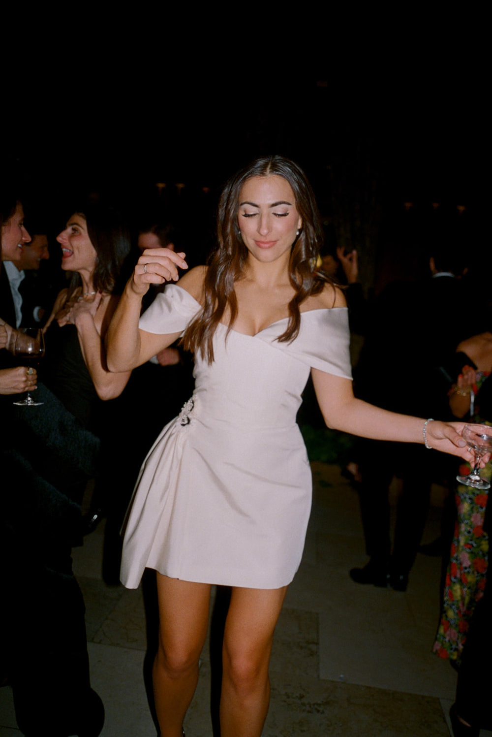 Bride dancing in a white off-the-shoulder dress at a dimly lit wedding after-party