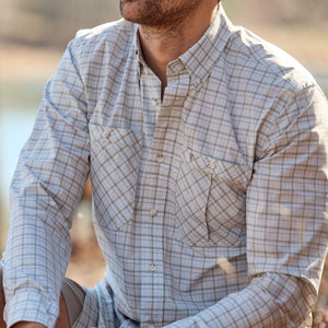 A man in a plaid Tom Beckbe Tidewater Shirt sits outdoors with a blurred natural background, face partially visible.