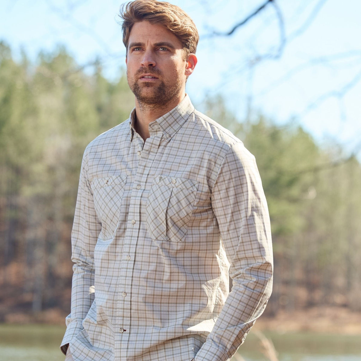 A man in a Tom Beckbe Tidewater Shirt with UPF 30+ stands outdoors with trees and a clear sky behind him.