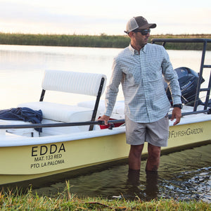 Man in water wearing a Tom Beckbe Tidewater Shirt holds a yellow boat named EDDA; reeds in background.