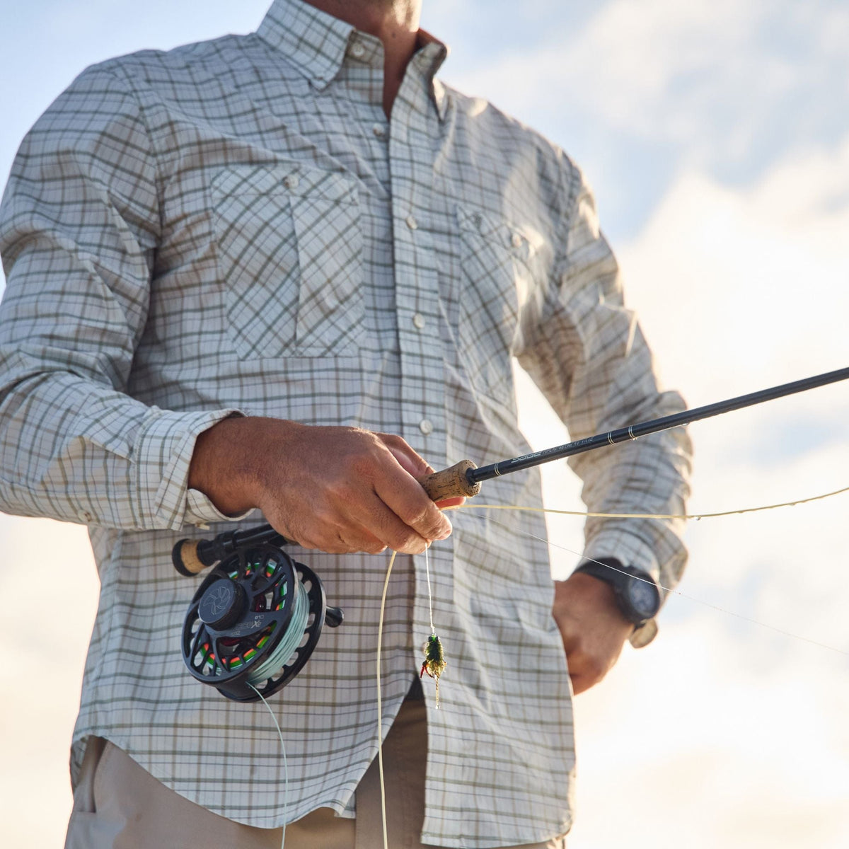 Under a partly cloudy sky, someone in a Tom Beckbe Tidewater Shirt enjoys fishing with UPF 30+ protection.