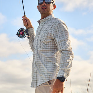 Man in sunglasses, wearing a Tom Beckbe Tidewater Shirt, holds a rod under a partly cloudy sky.