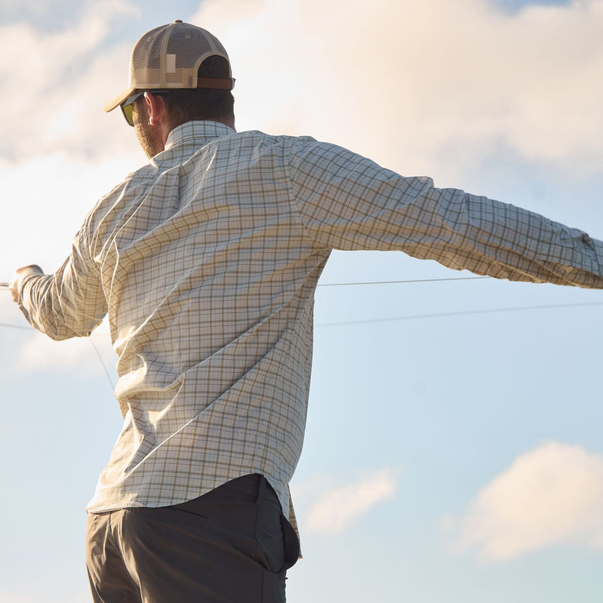Someone in a Tom Beckbe Tidewater Shirt and cap casting under a clear sky.