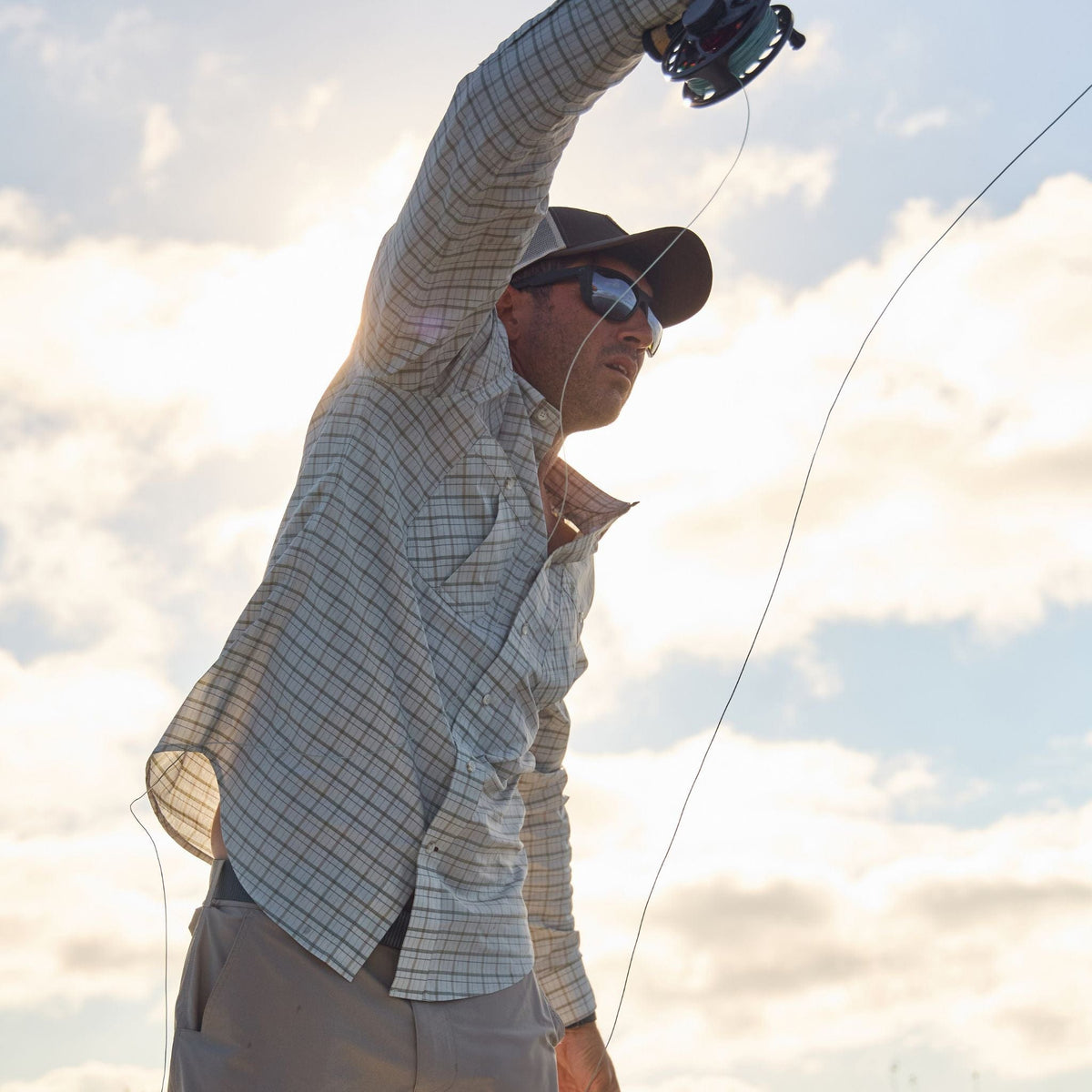 Person in a Tom Beckbe Tidewater Shirt and cap fly fishing under a partly cloudy sky.