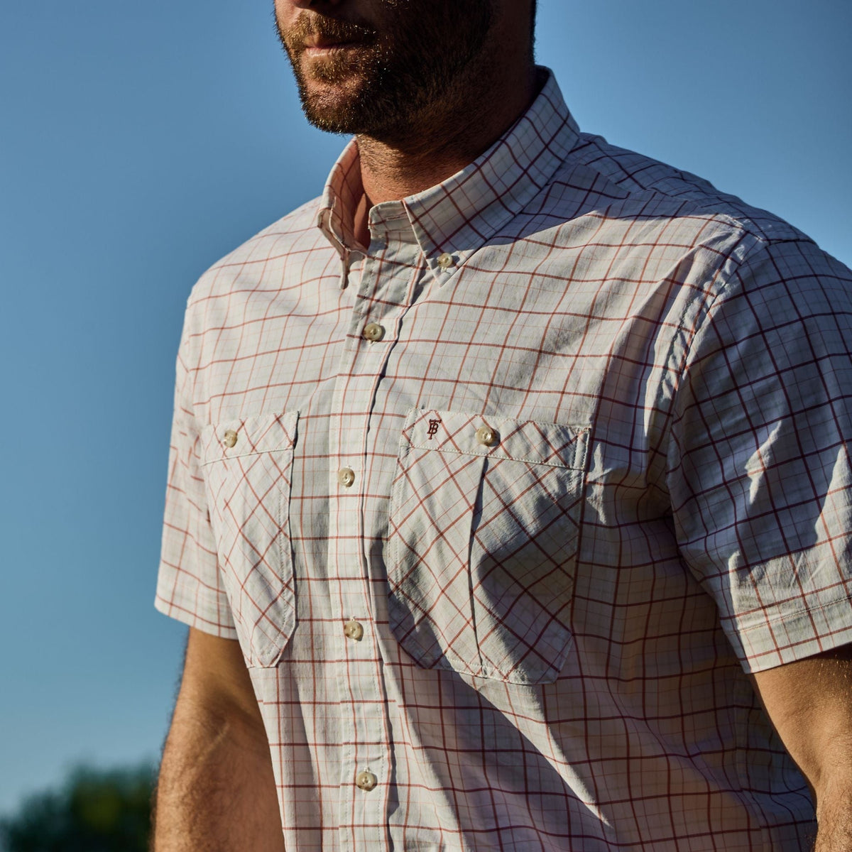Man in a Tom Beckbe Tidewater Shirt (Short Sleeve) standing outdoors against a clear blue sky.
