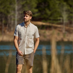 A man in a Tom Beckbe Tidewater short-sleeve shirt stands near a lake with trees in the background.