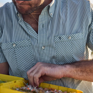 A person in a Tom Beckbe Tidewater Shirt inspects fishing flies in a yellow tackle box.