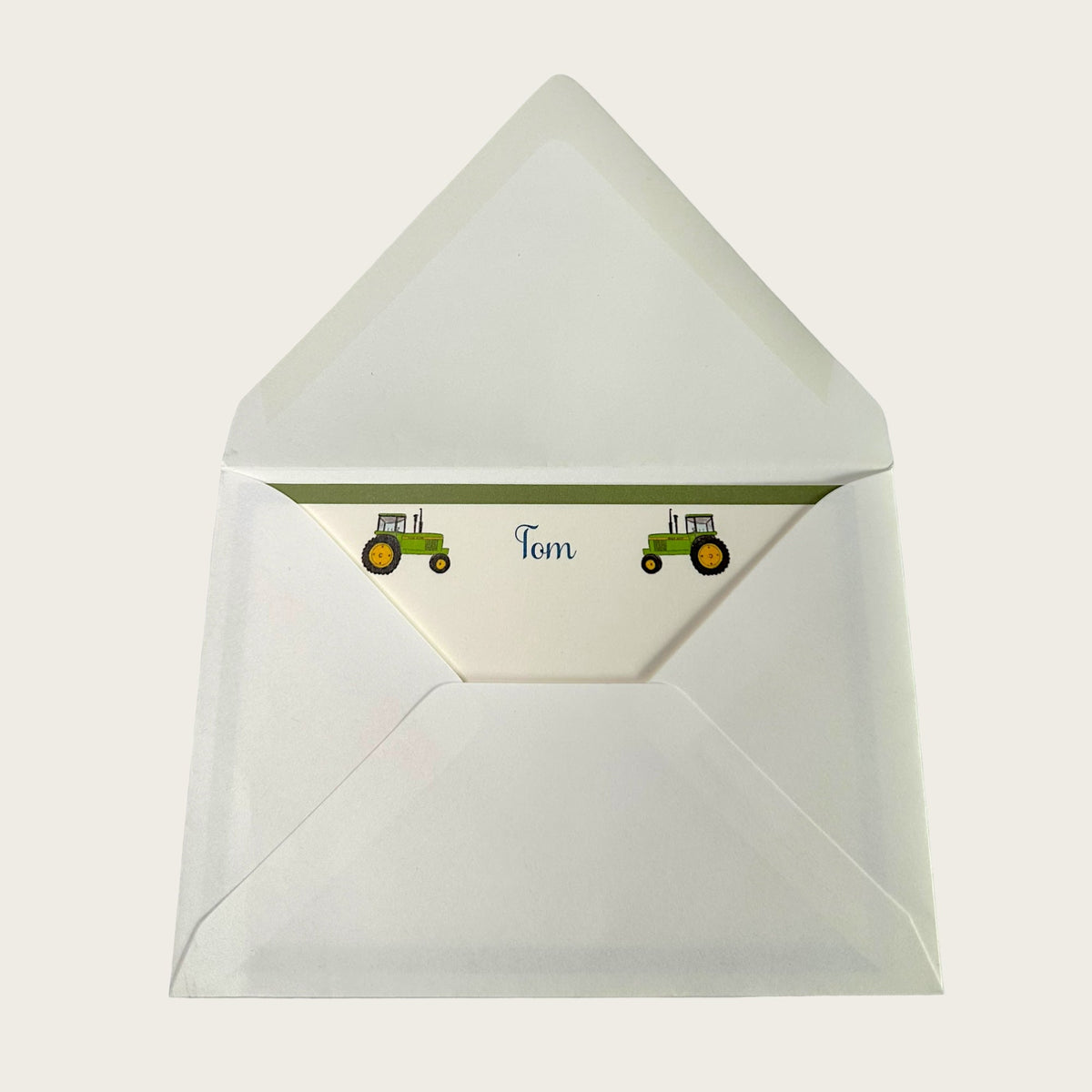 Top view of opened tractor notecard envelope showing personalized liner with two green tractor illustrations and the name Tom