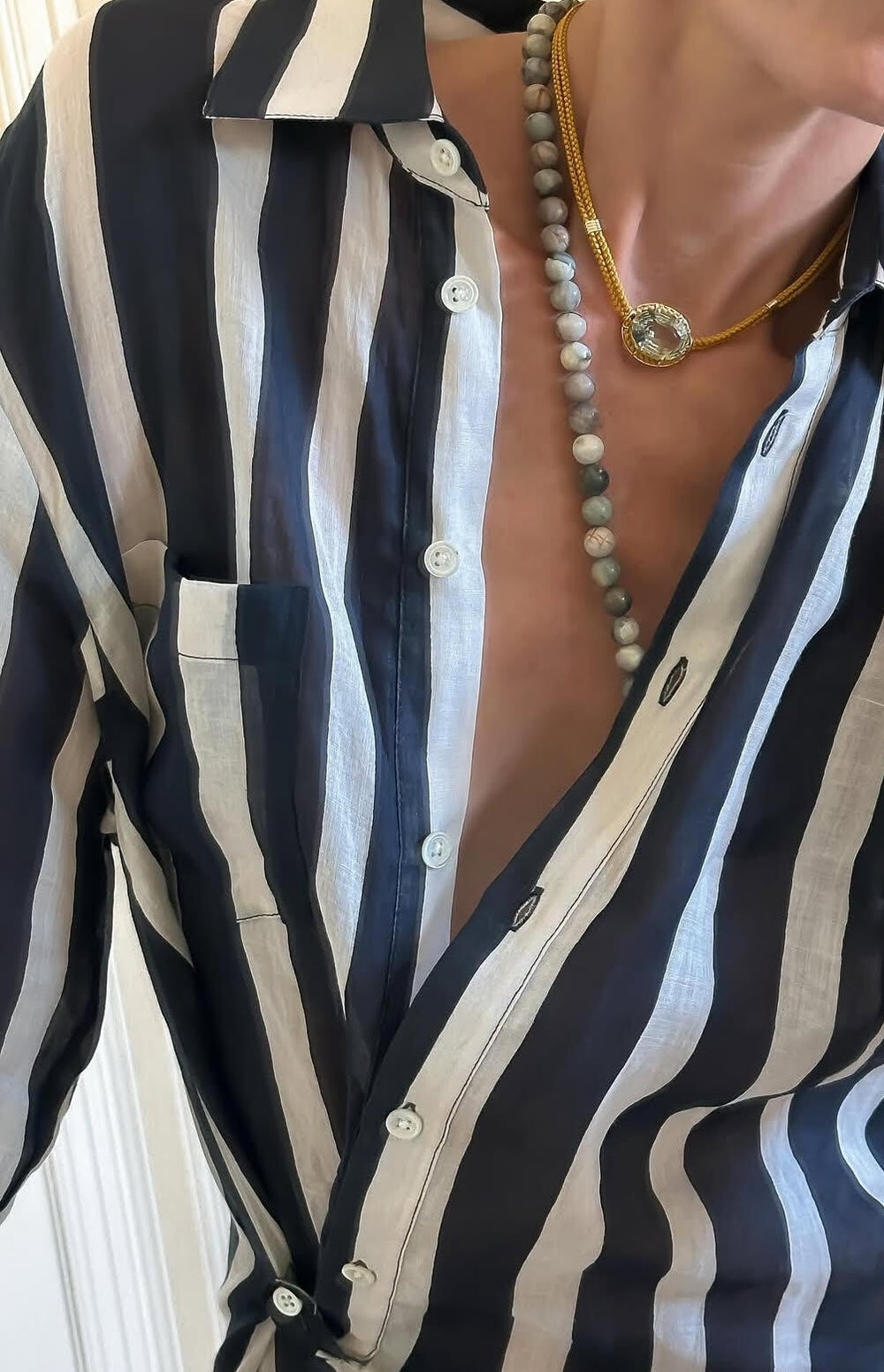 Close up of Green Amethyst pendant on ochre silk cord with 18K yellow gold bezel, worn with black and white striped shirt
