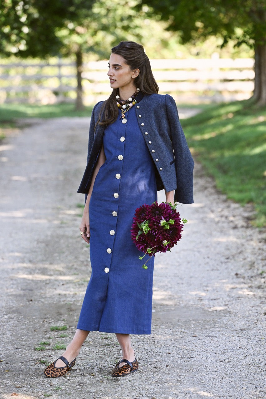 Model wearing Vermont Bubble Necklace with navy jacket, standing on a tree-lined gravel path holding a dark purple bouquet