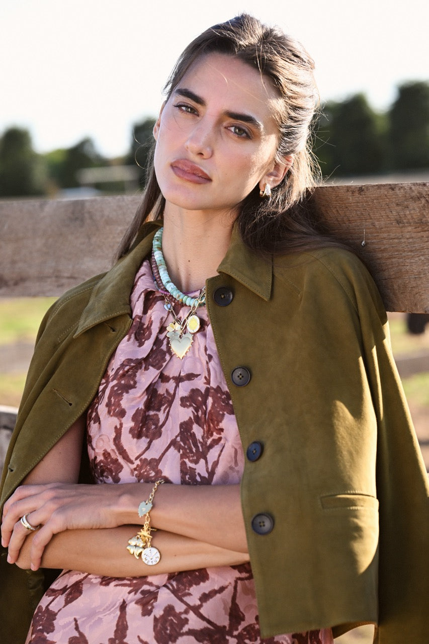 Model wearing Gardenia diamond hoop earrings leaning against a wooden fence outdoors, wearing an olive jacket and pink floral dress