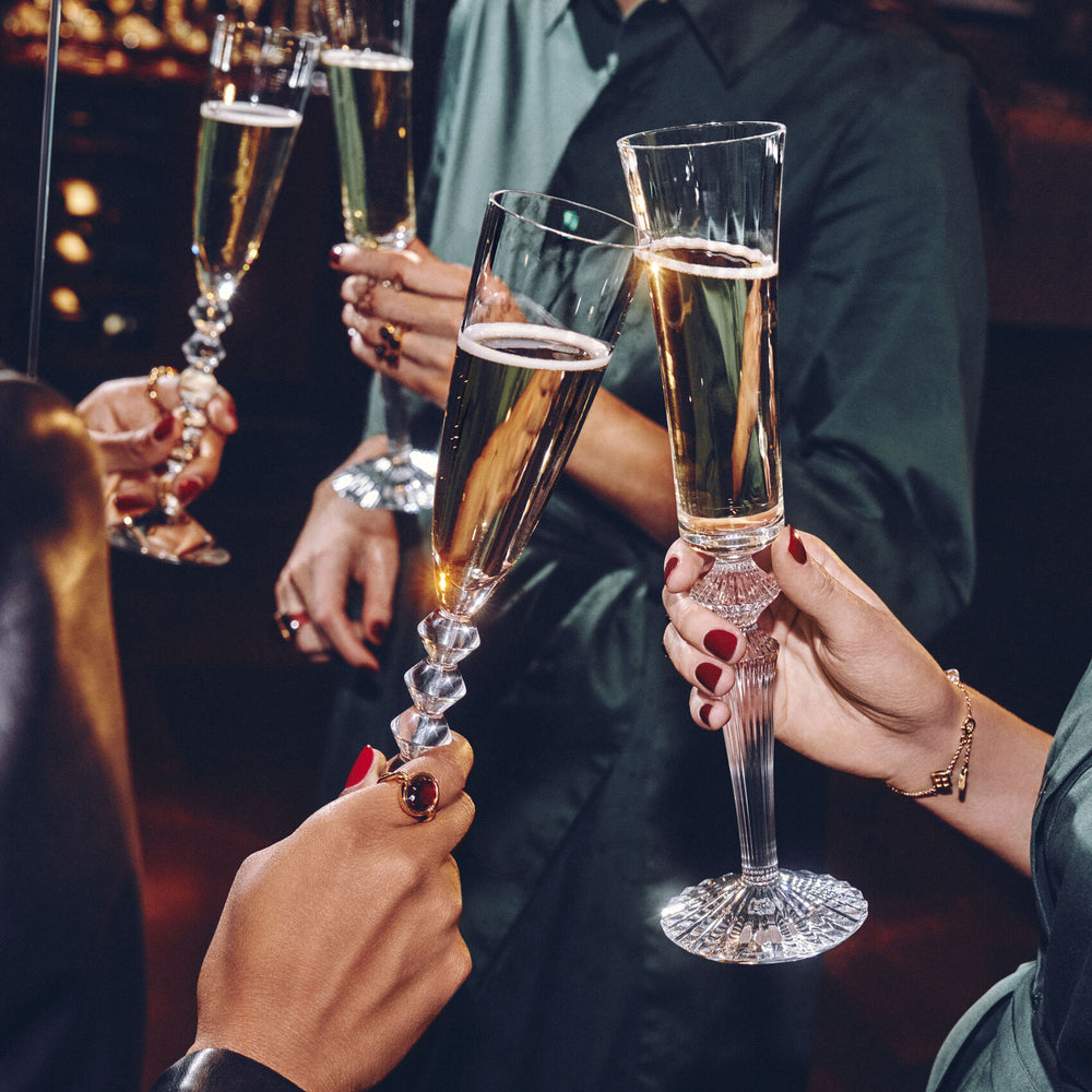Four people toasting with Mille Nuits Flutissimo crystal champagne flutes in a dim, festive bar setting