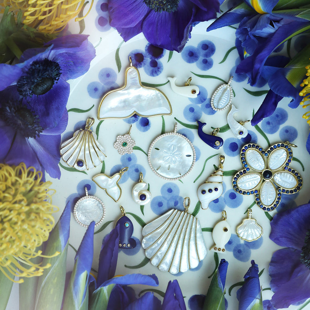 Top-down view of Ivory Moby charm showcasing faux ivory whale silhouette with 14K gold-dipped edge and tiger’s-eye cabochon eye on a floral plate background