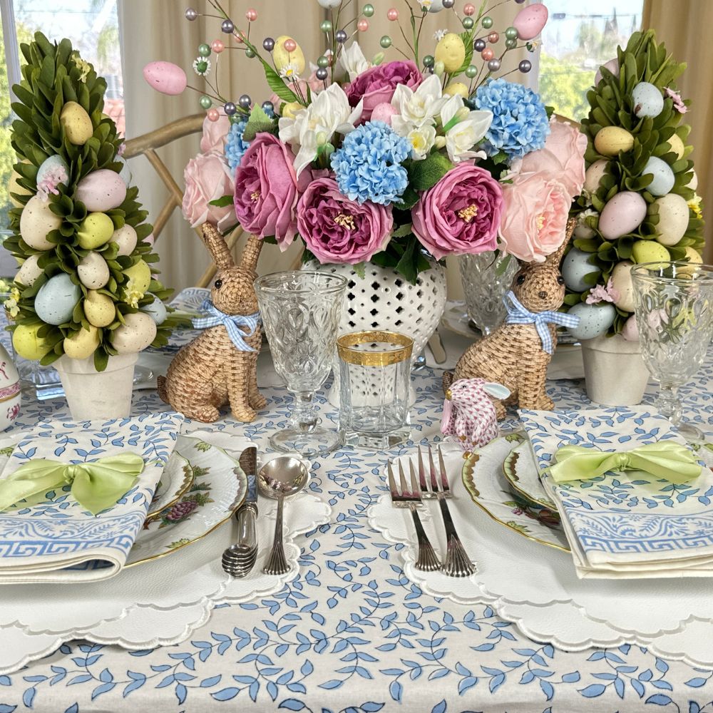 Easter-themed table setting with floral centerpieces, bunny decorations, and colorful eggs.