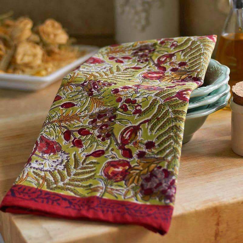Angled view of Winter Garden Wreath Tea Towels Red and Green, Set of 3 with floral pattern draped over stacked dishes