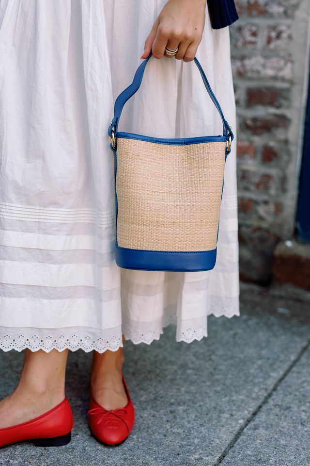 Front view of Boo Tote in rattan showcasing woven body and navy leather trim, held by a model against a white skirt